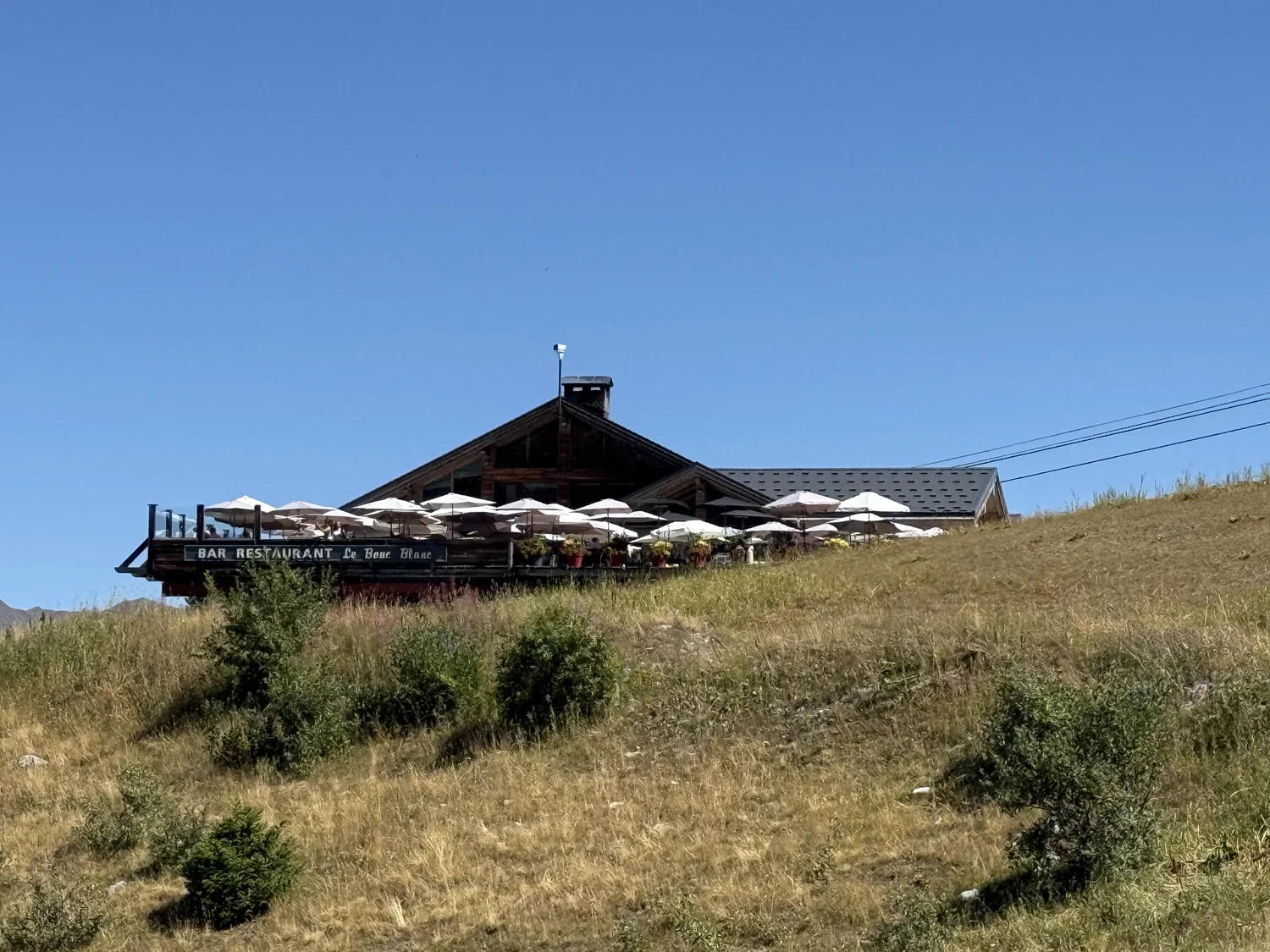 Chalet en bois du bar-restaurant Le Bouc Blanc et ses parasols, vu depuis la pente