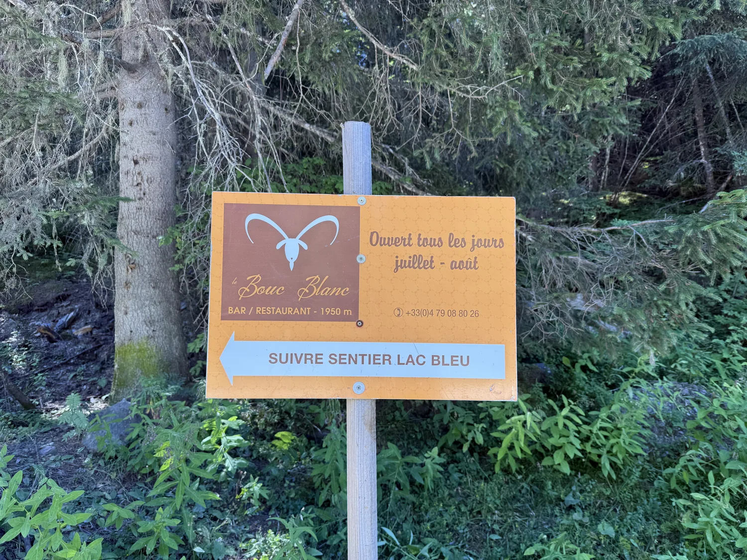 Panneau orange du bar-restaurant Le Bouc Blanc indiquant 1950 m et le sentier du Lac Bleu