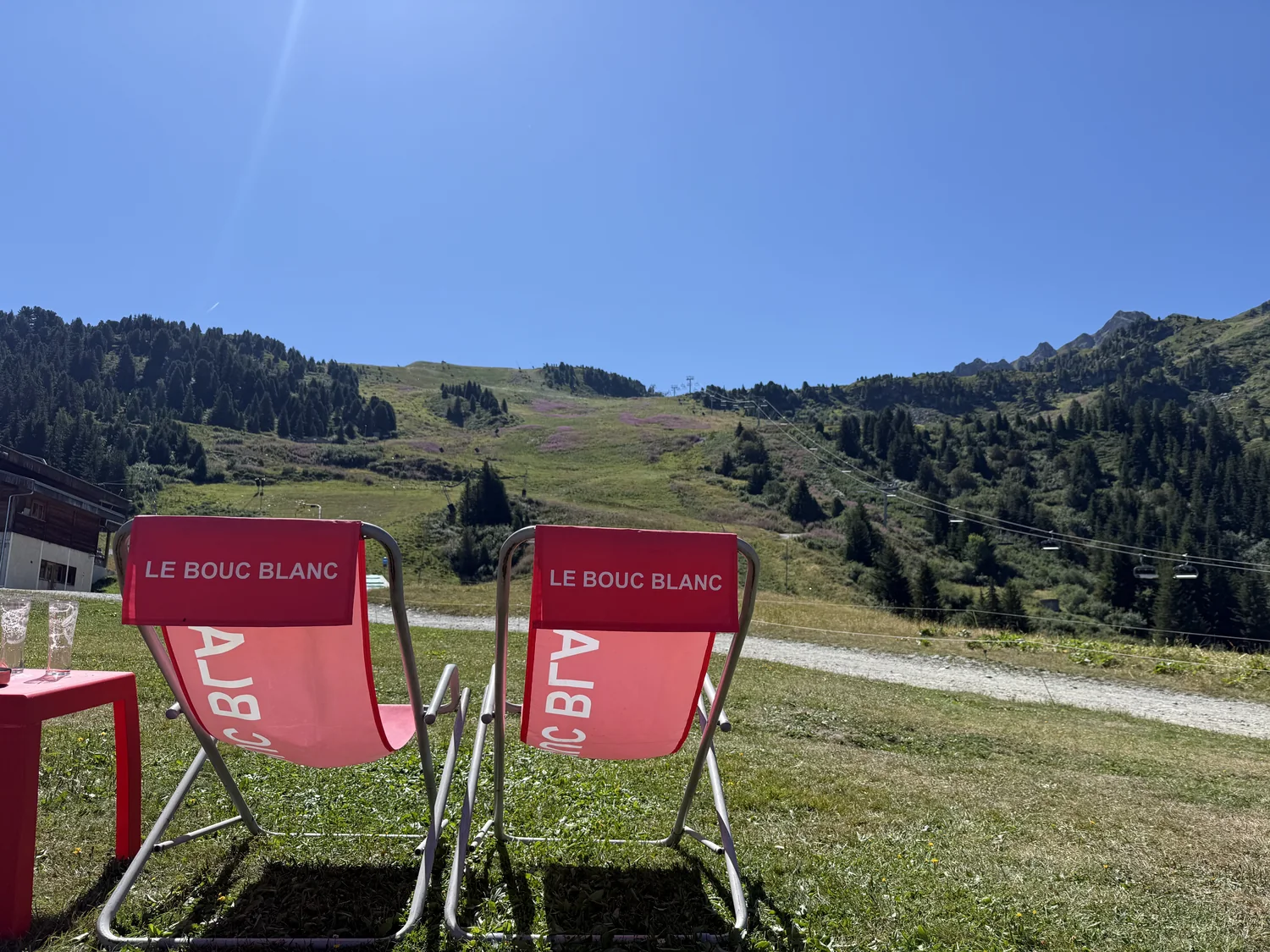 Deux transats rouges marqués Le Bouc Blanc installés dans l'herbe face à la montagne