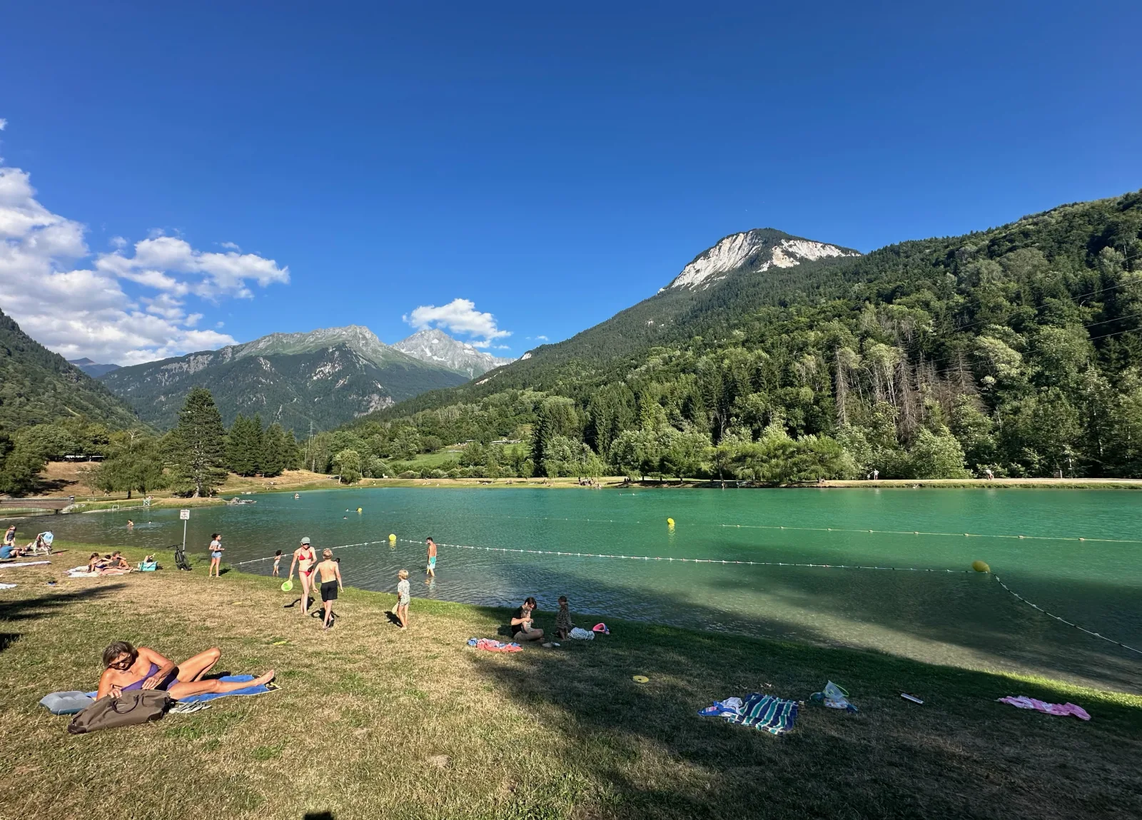 Grass beach at the Bozel lake, towels spread out and swimmers