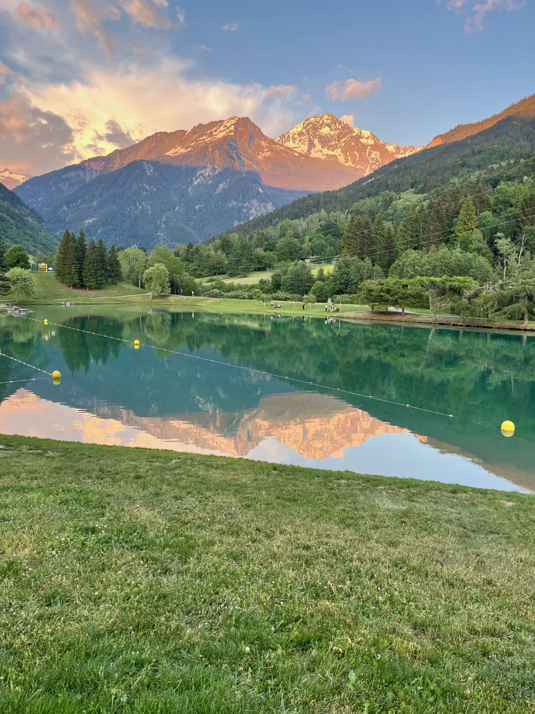 Swimming area marked out by yellow buoys at the Bozel lake, wide lawn in the foreground